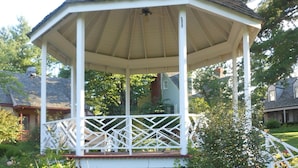 A gazebo with a white lattice railing, surrounded by a garden with various plants and flowers. - Century Suites Hotel (Bloomington)