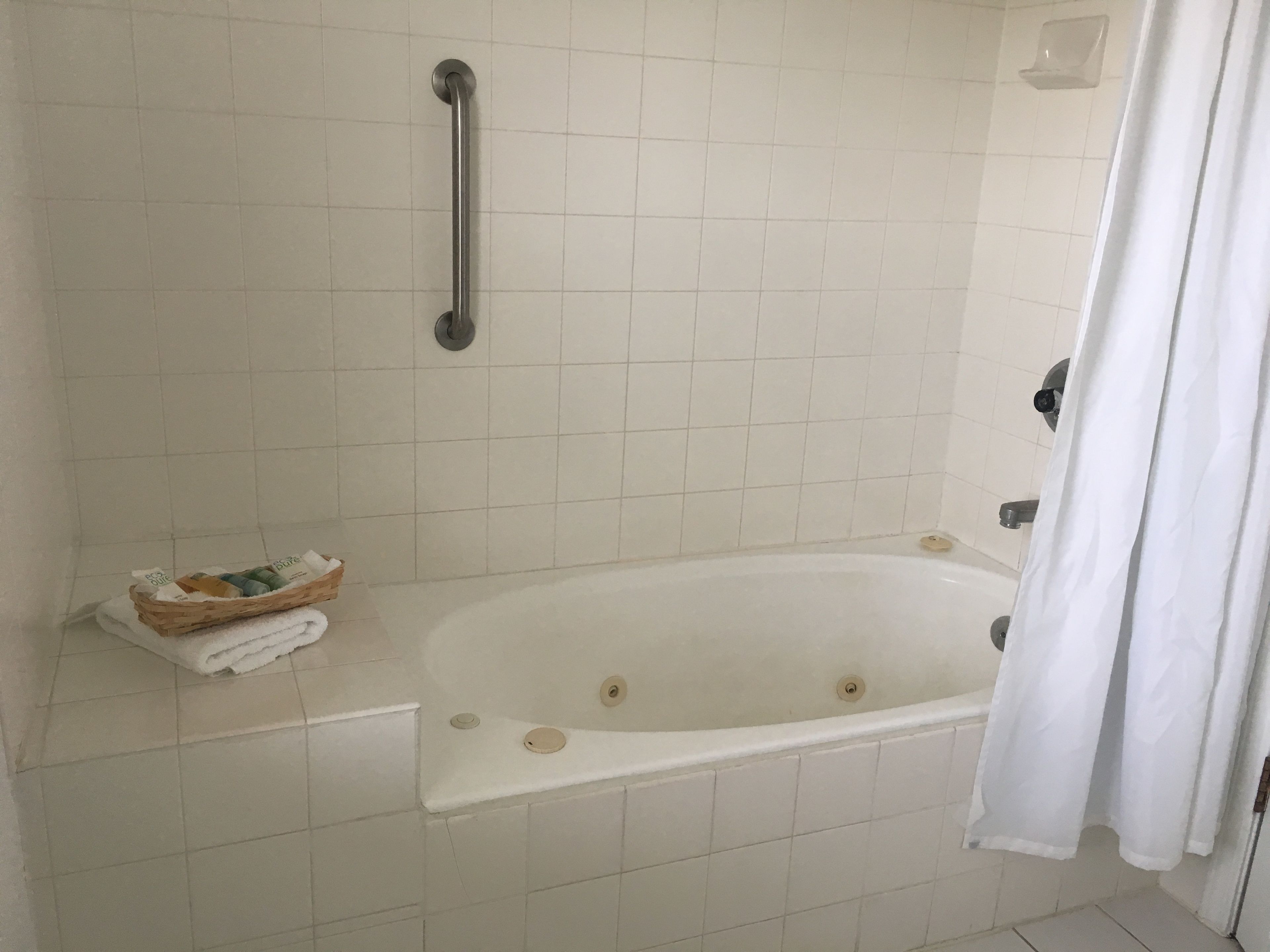 Un baño con bañera, barra de apoyo, perchero y una cesta pequeña con artículos de aseo.
