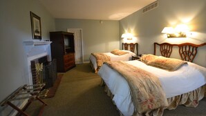 A hotel room with two beds, a fireplace, a wardrobe, and wall-mounted lamps. - Century Suites Hotel (Bloomington)