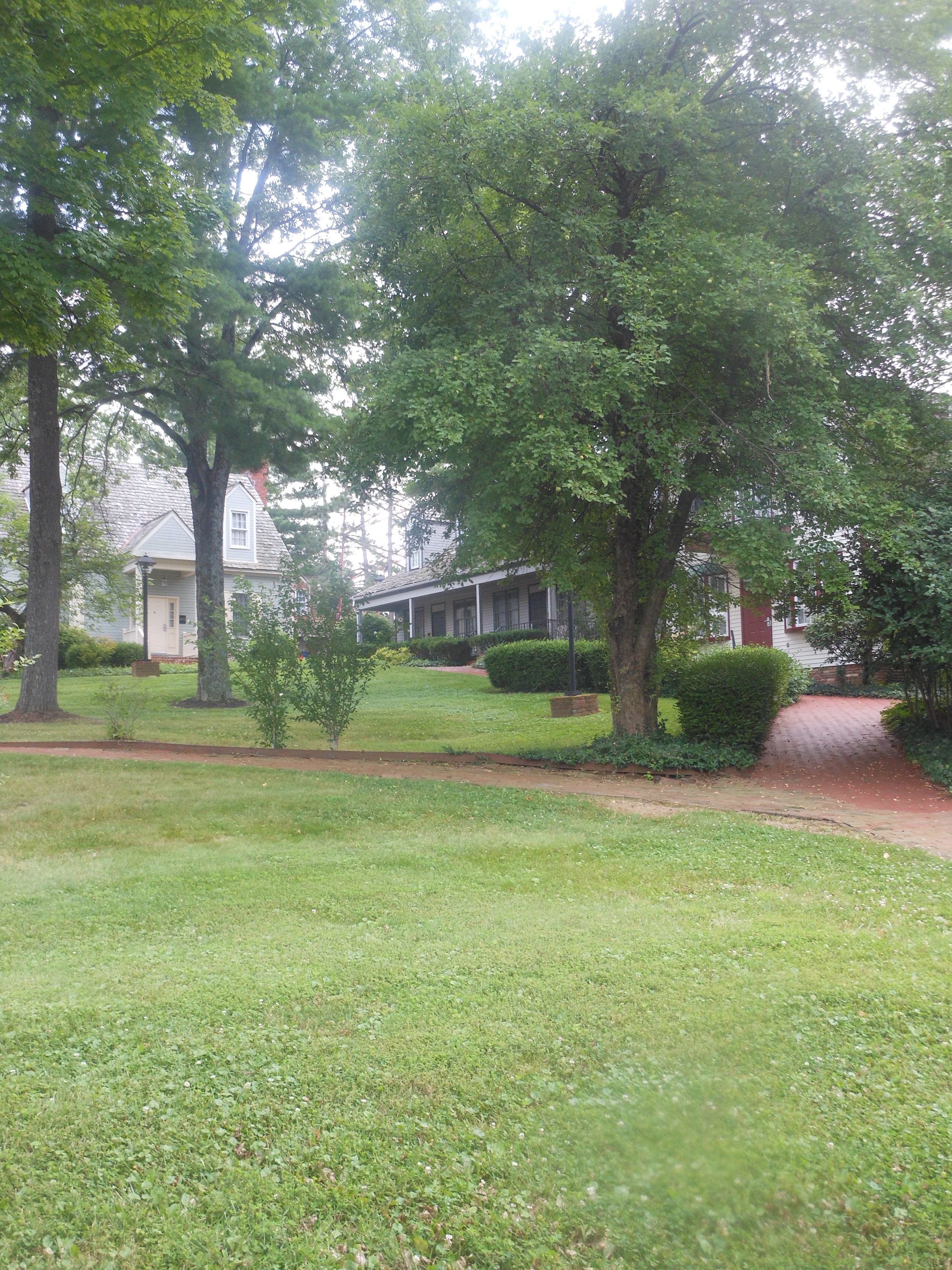 A residential property with a well-maintained lawn, mature trees, and a house with a porch.