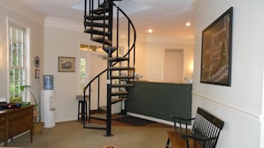 A spacious room with a spiral staircase, a dining area with wooden chairs, a water dispenser, and a green cushioned bench. - Century Suites Hotel (Bloomington)