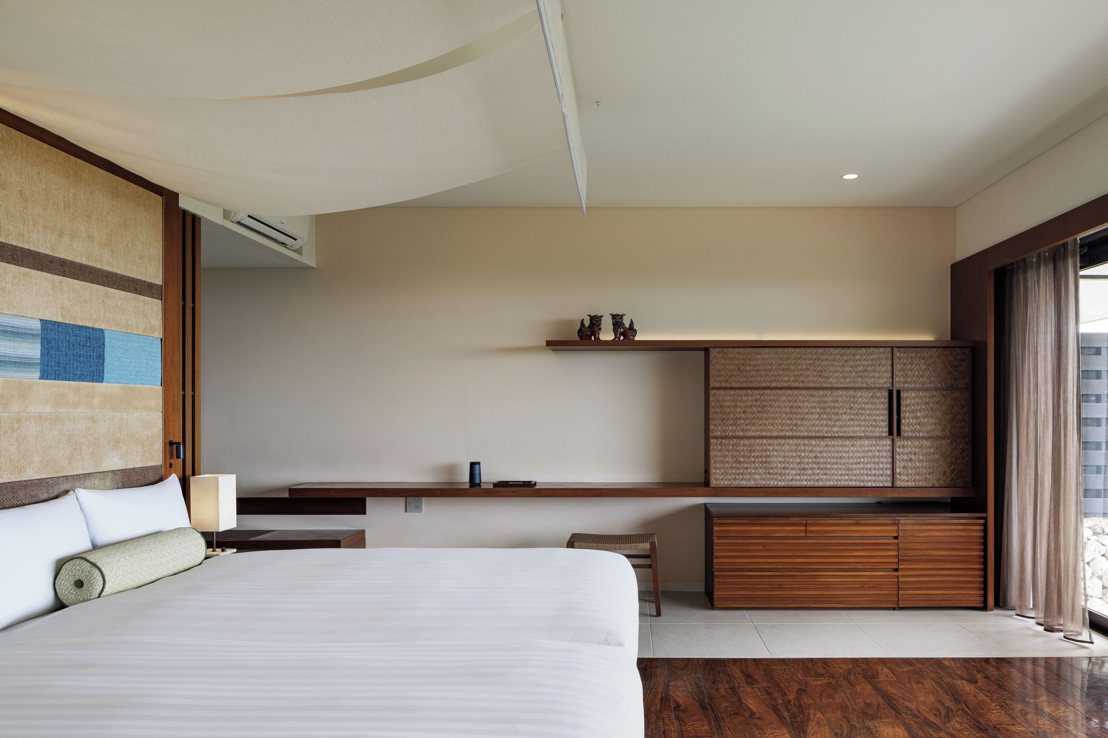 A modern hotel room with a large bed, a wooden cabinet, a small table, and a wall-mounted shelf.