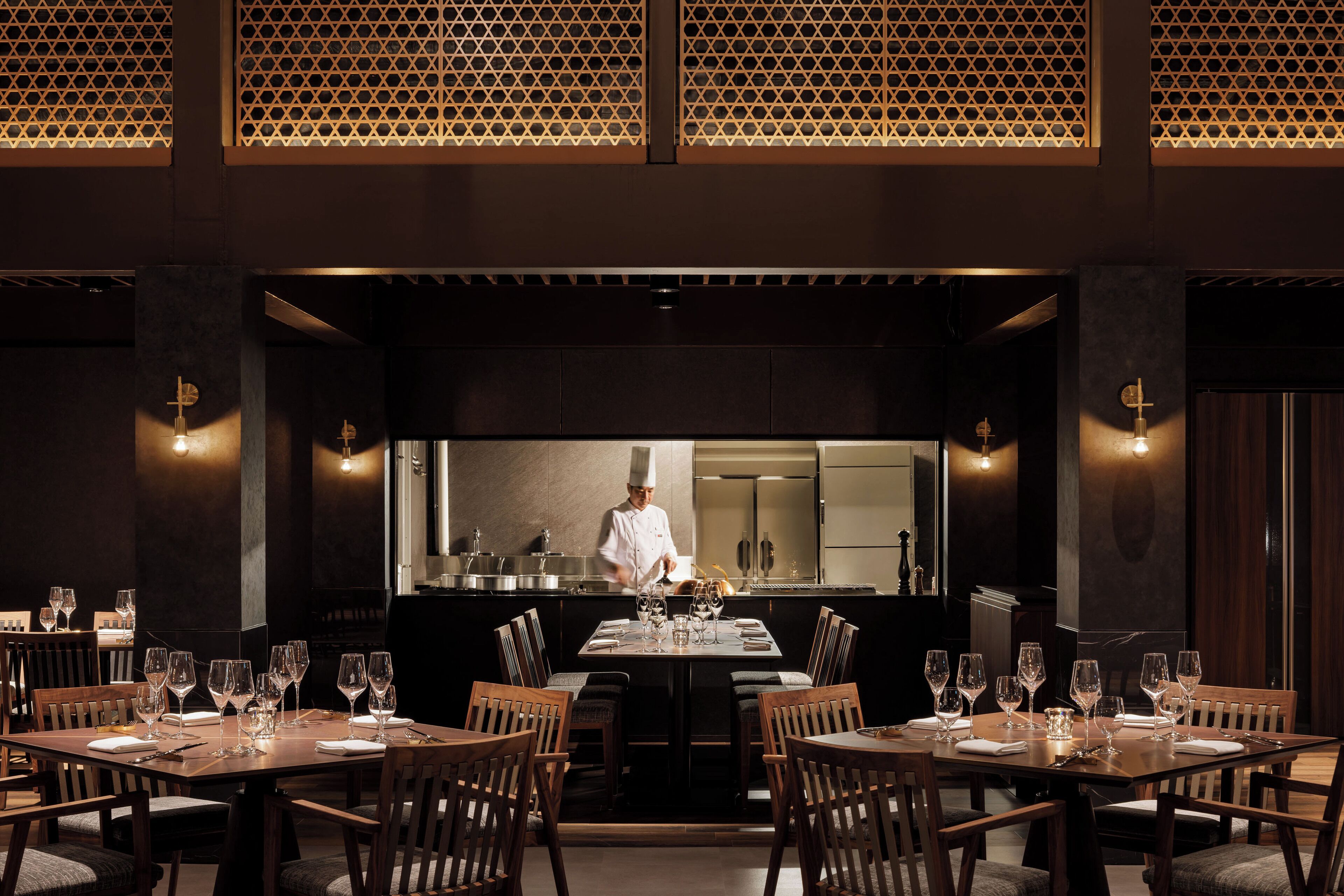 A restaurant with a chef preparing food in the background, wooden tables and chairs, and a modern interior design.
