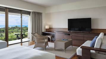 A modern hotel room with a large bed, a sofa, a TV, and a balcony with a view of the sea.