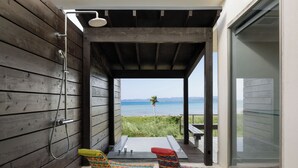 A wooden room with a shower, two colorful chairs, a table, and a view of the ocean.