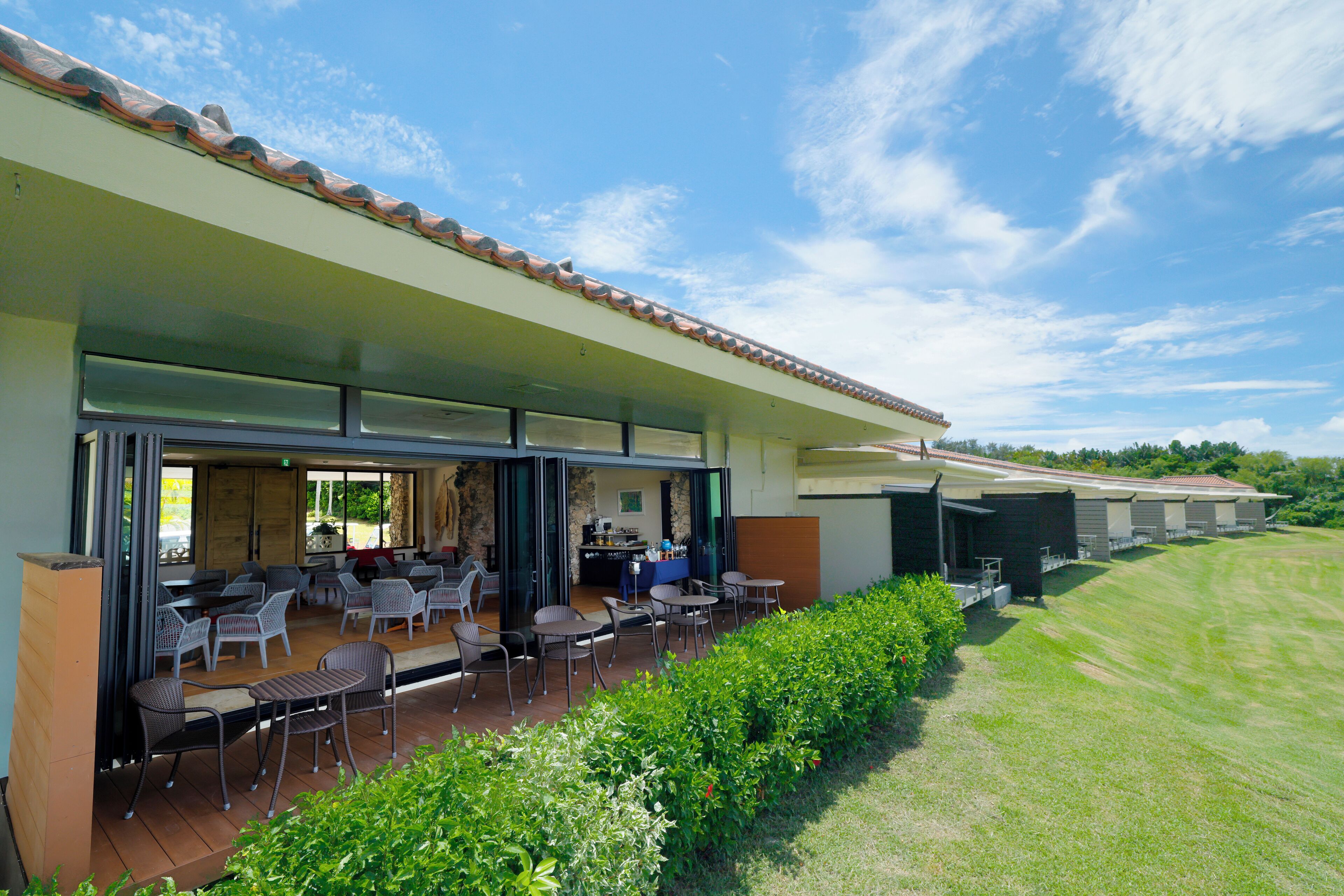 An outdoor patio area with tables and chairs, a bar, and a view of a green landscape.