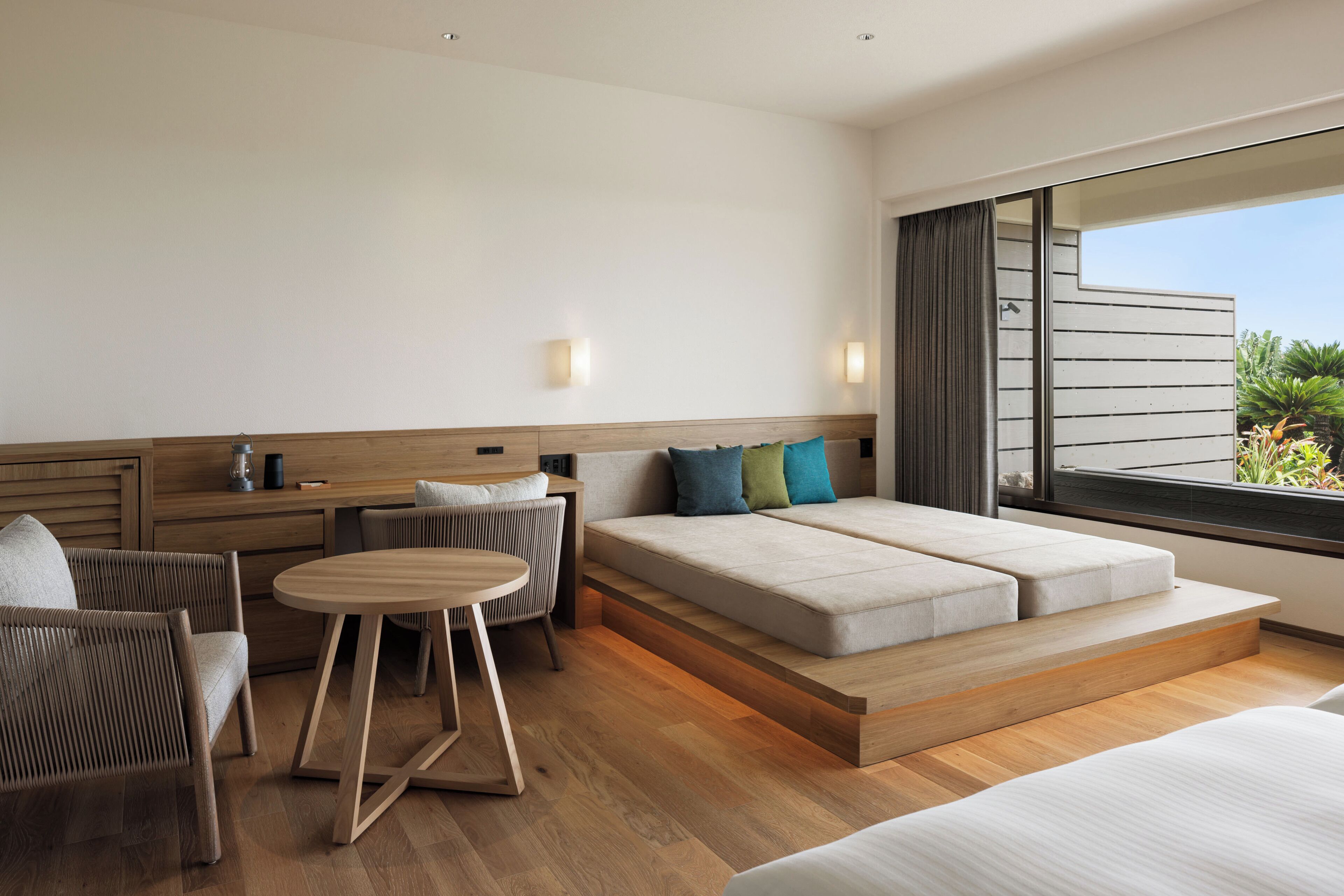 Une chambre d’hôtel moderne, dotée d’un canapé, de fauteuils, d’une petite table et d’une grande fenêtre donnant sur un paysage verdoyant.