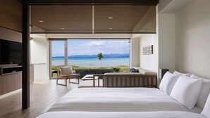 A modern hotel room with a large bed, a seating area with a view of the ocean, and a television.