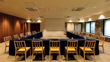 Una sala conferenze con un lungo tavolo, sedie e un muro in pietra con finestre.