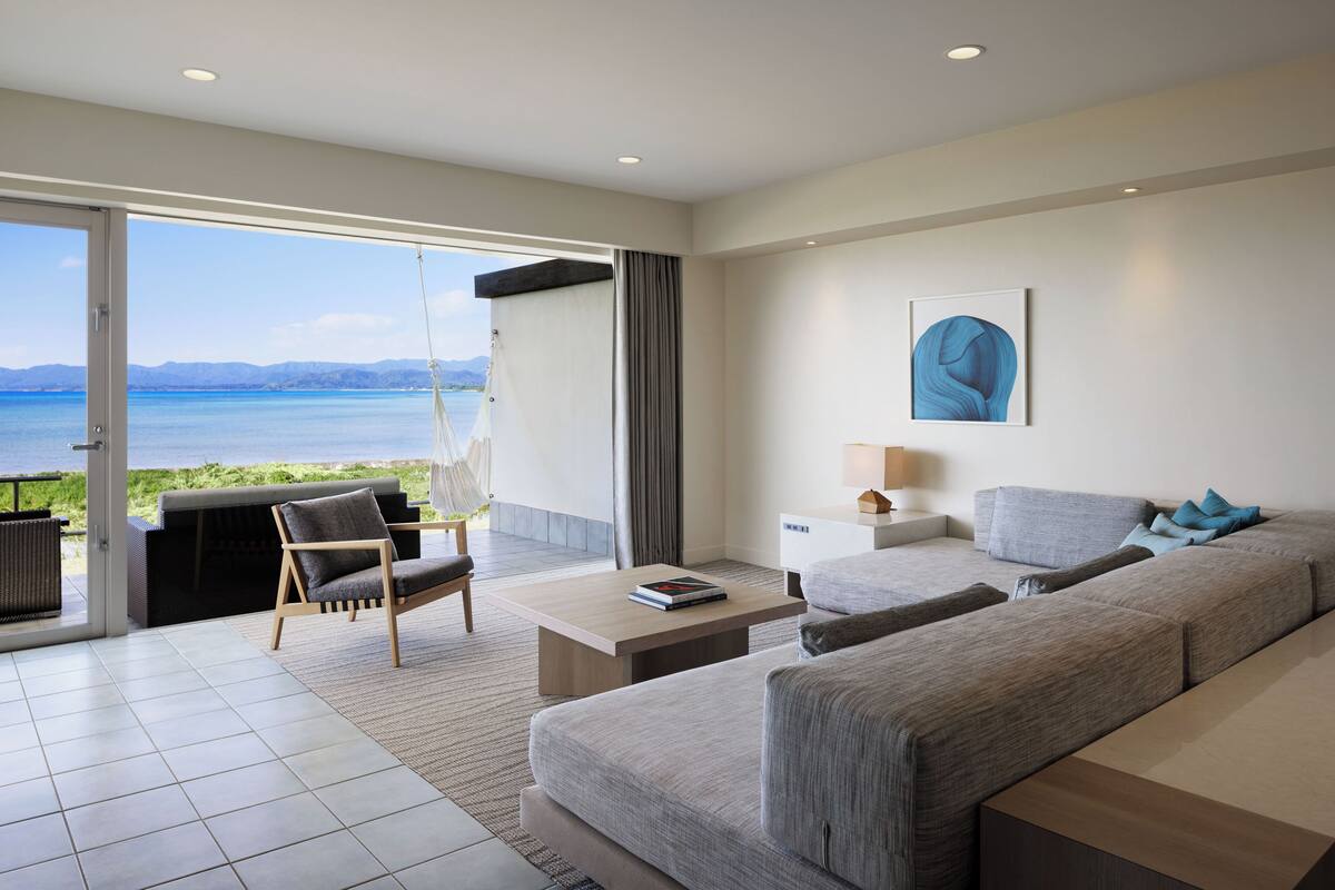 A modern living room with a sofa, a chair, a coffee table, and a view of the sea.