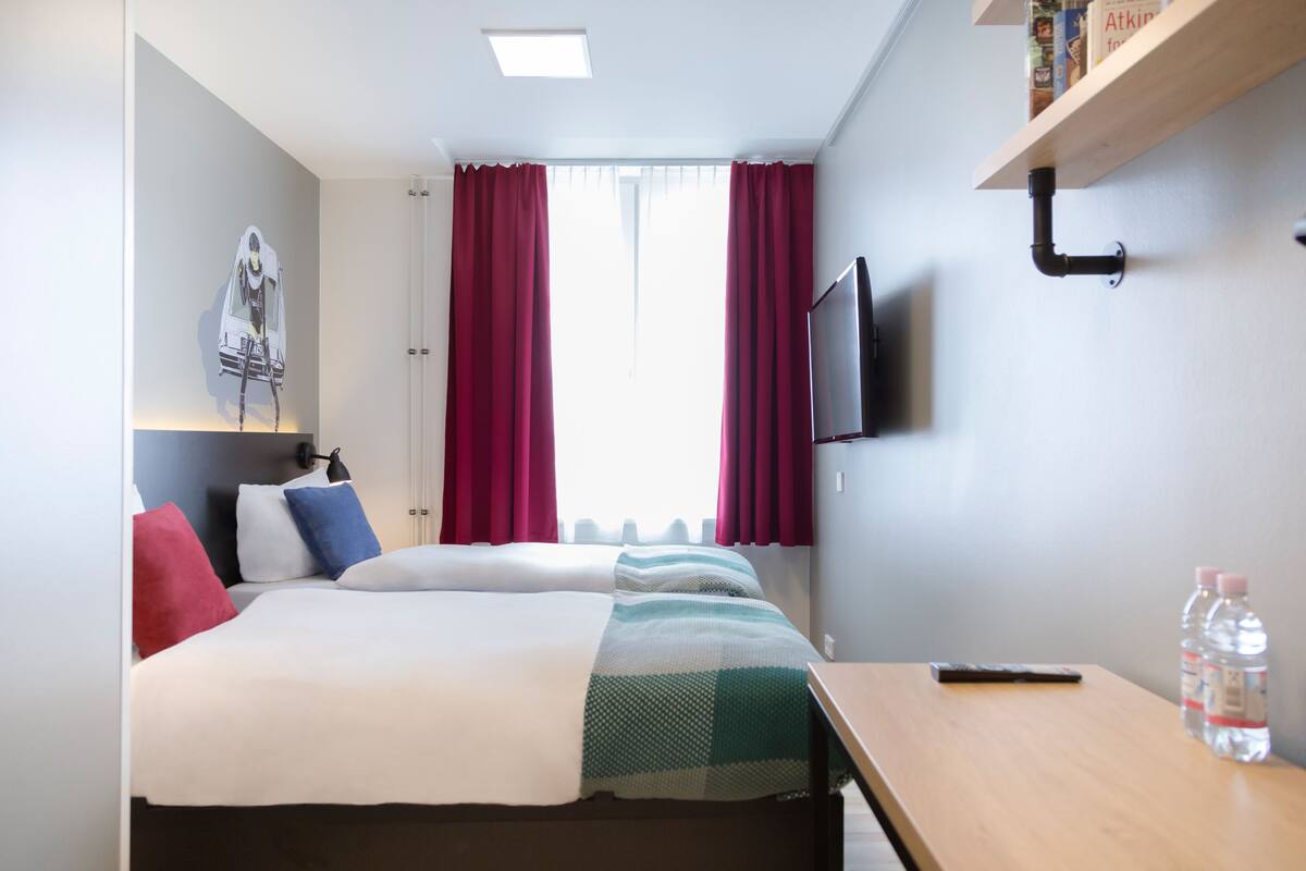 A hotel room with a bed, a desk, a TV, and a window with curtains.
