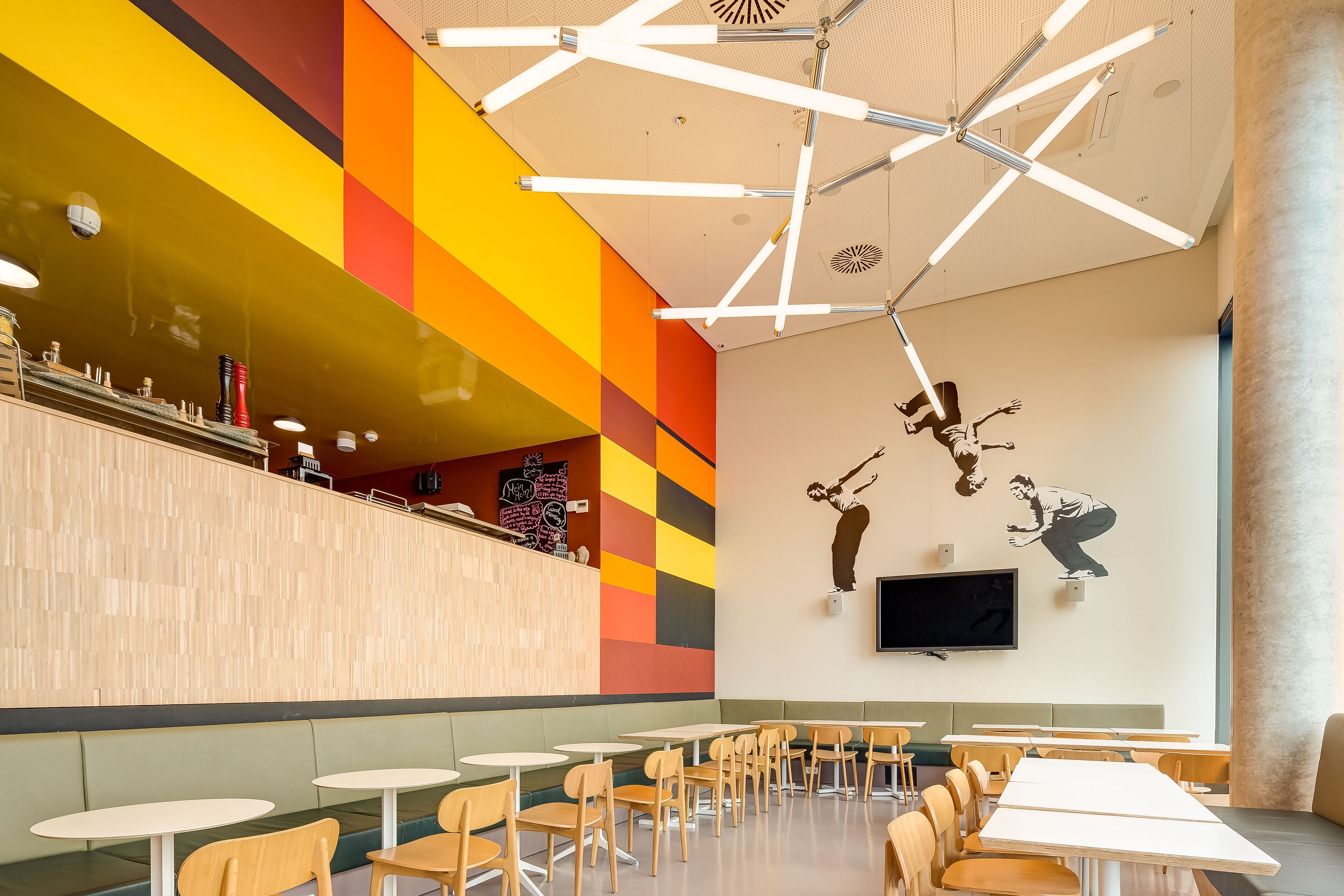 A modern cafe with a vibrant wall mural, a wooden counter, and multiple seating areas.
