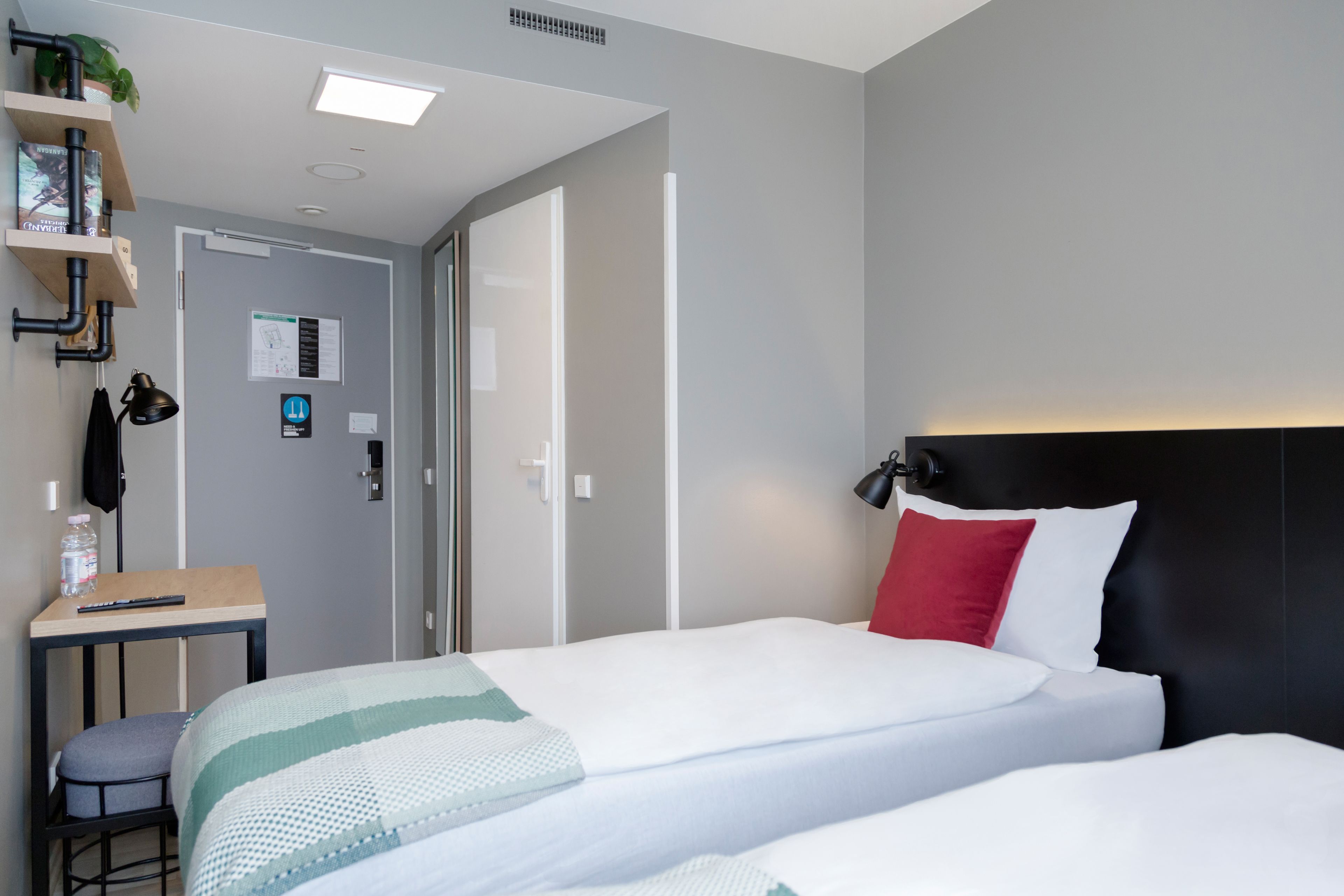 A modern hotel room with a bed, bedside table, and a desk with a chair.