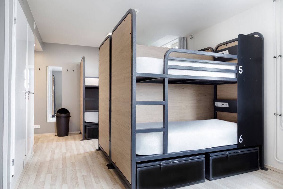 A bunk bed room with a wooden floor, a black metal frame, and a small trash bin.
