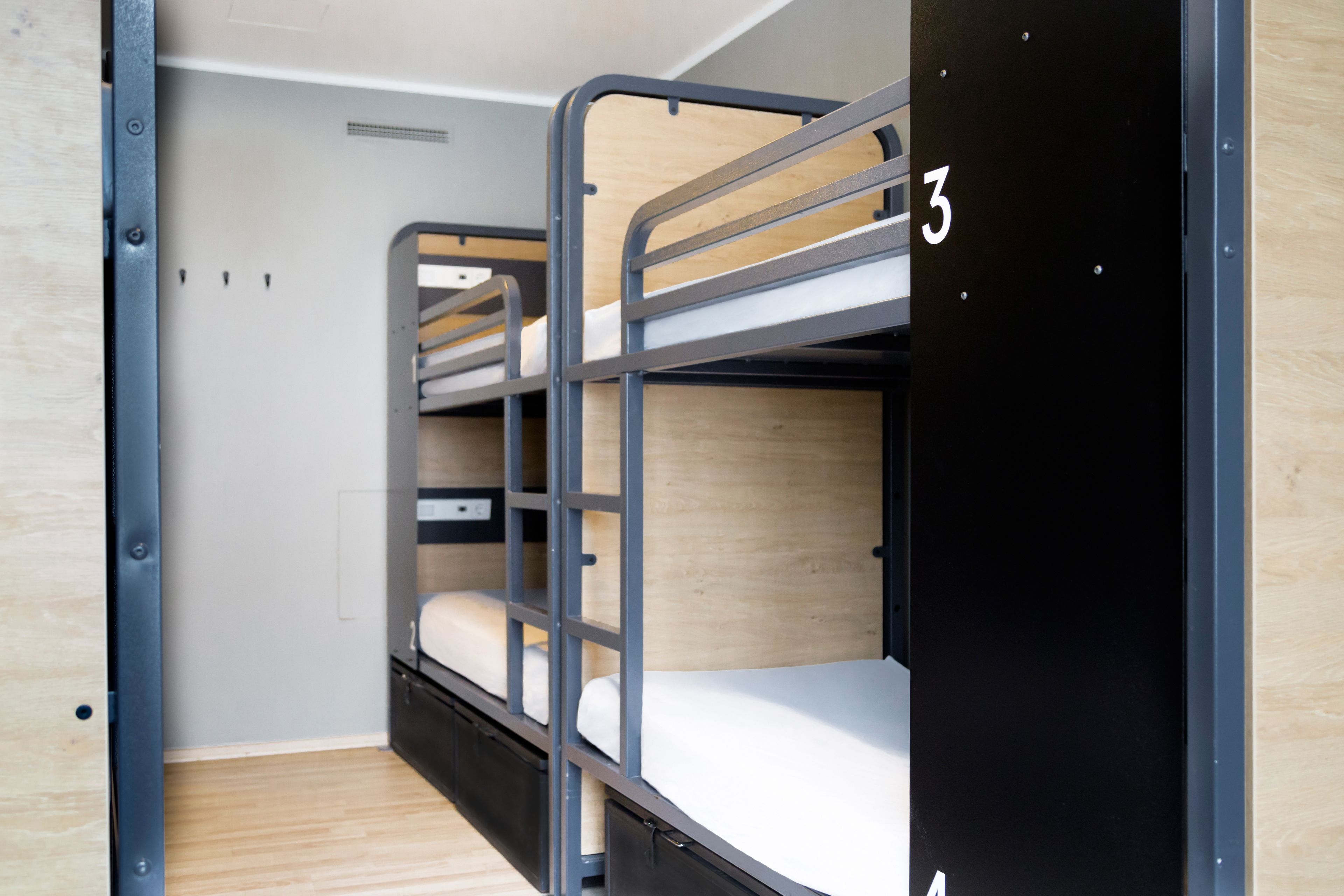 Ein Schlafraum mit Etagenbetten und der Nummer 3 auf der Tür, Holzboden und einer grauen Wand.