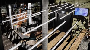 A modern bar area with a long counter, multiple hanging light fixtures, and a television screen displaying 'LIVE'. - Generator Hamburg (Hamburg)