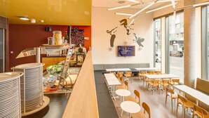 A modern cafe with a long counter, multiple tables, and chairs. - Generator Hamburg (Hamburg)