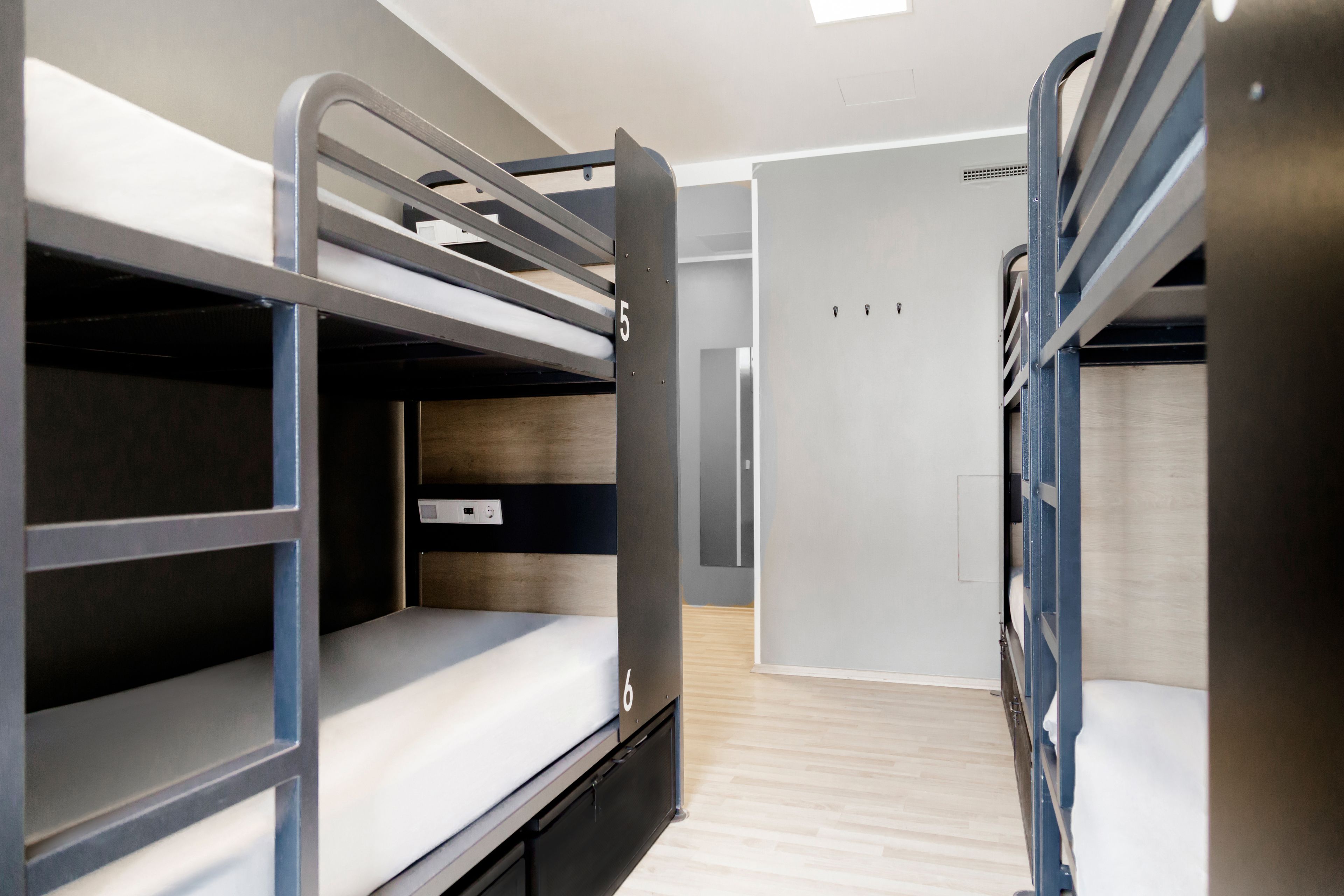 A bunk bed room with a wooden floor, a door, and a light switch on the wall.