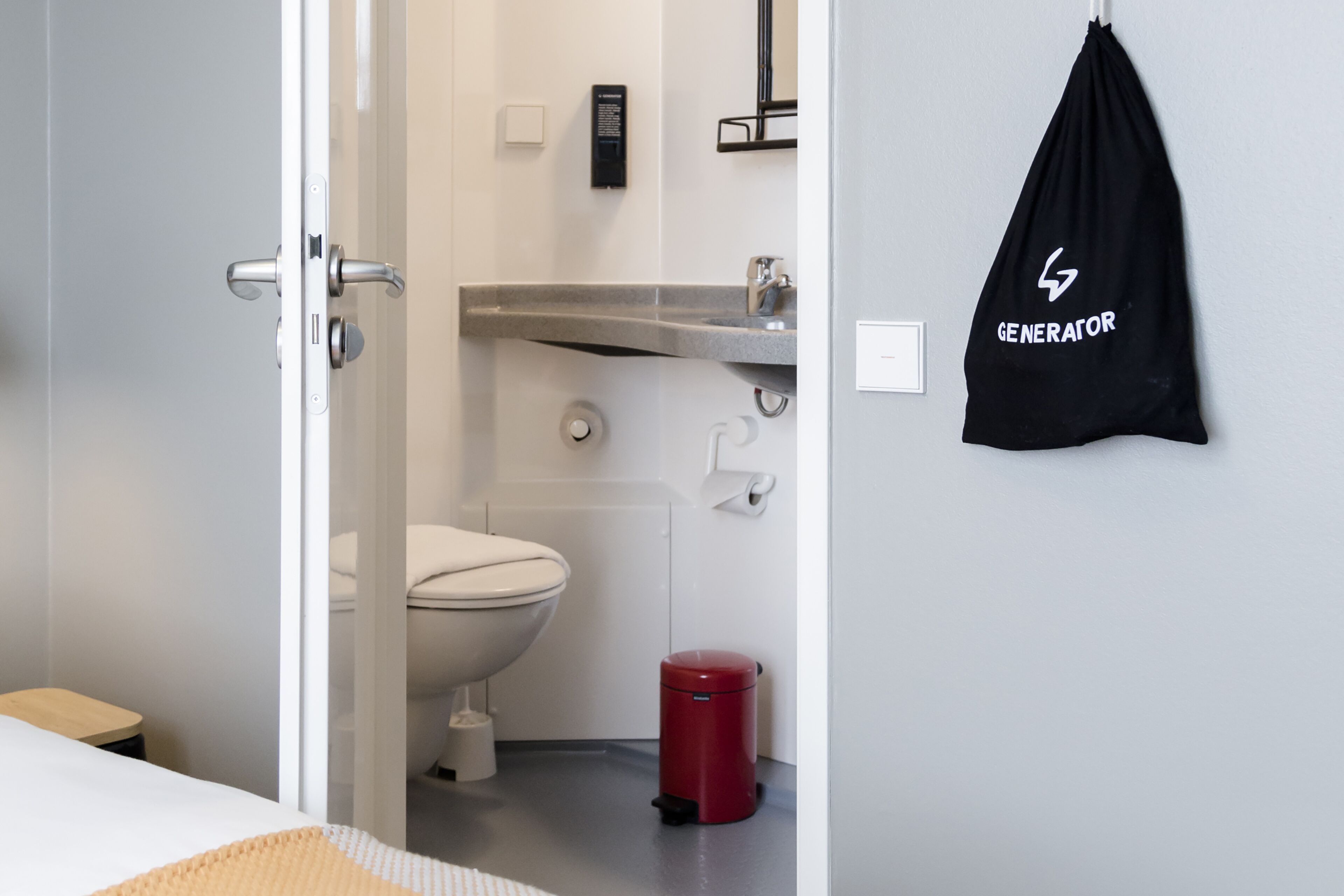 Une salle de bain moderne équipée de toilettes, d’un lavabo et d’une poubelle rouge.
