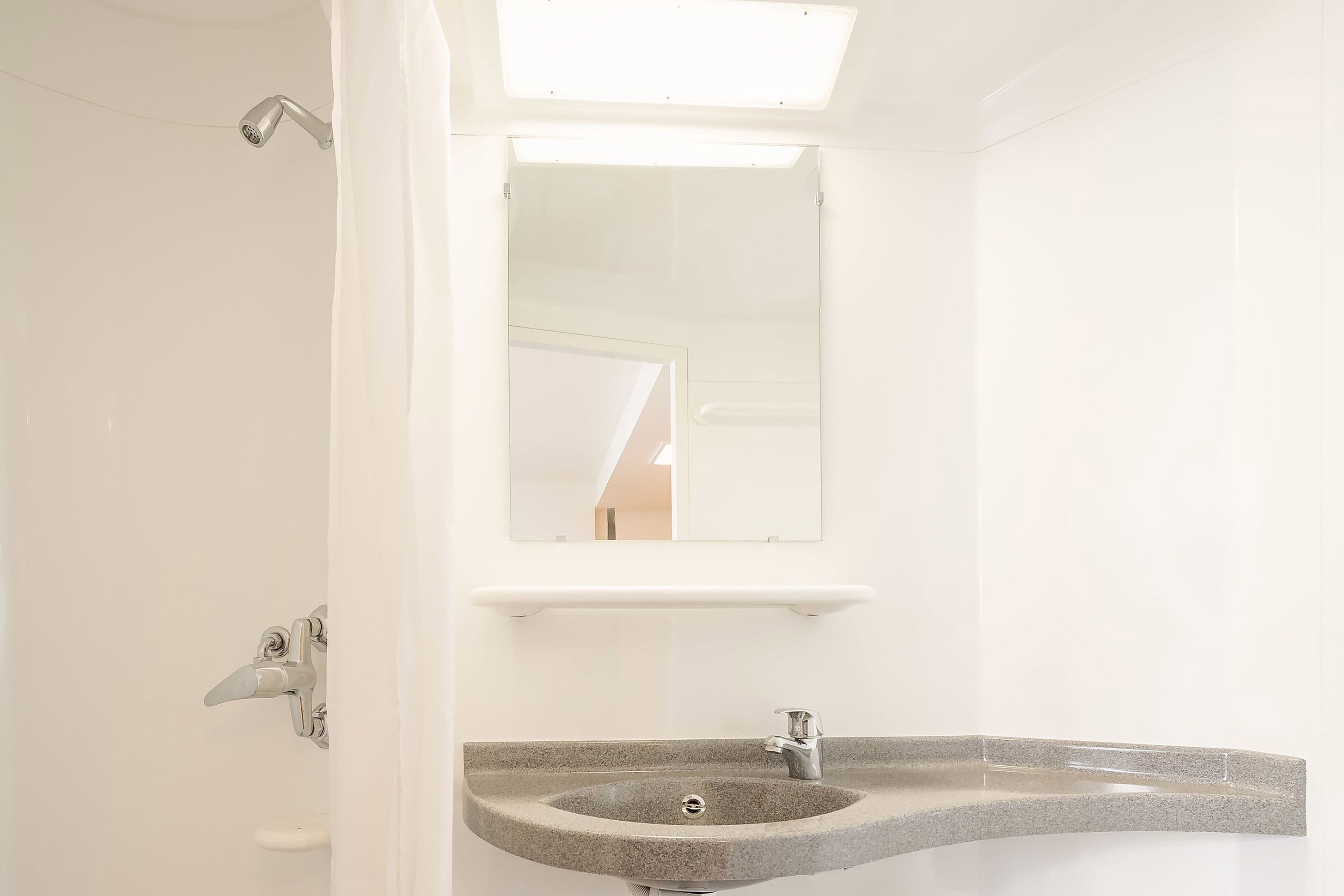 Un baño con lavamanos de granito, un espejo y un cabezal de ducha.
