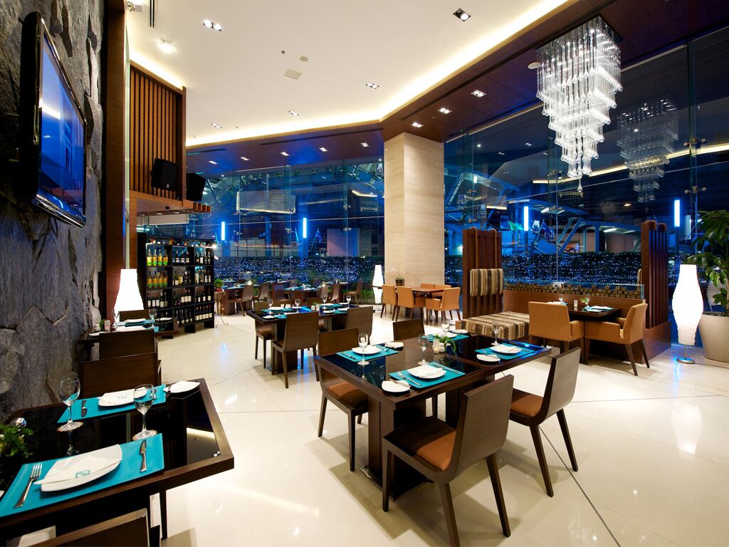 A modern hotel lobby with multiple dining areas, a bar, and a view of the cityscape through large windows.