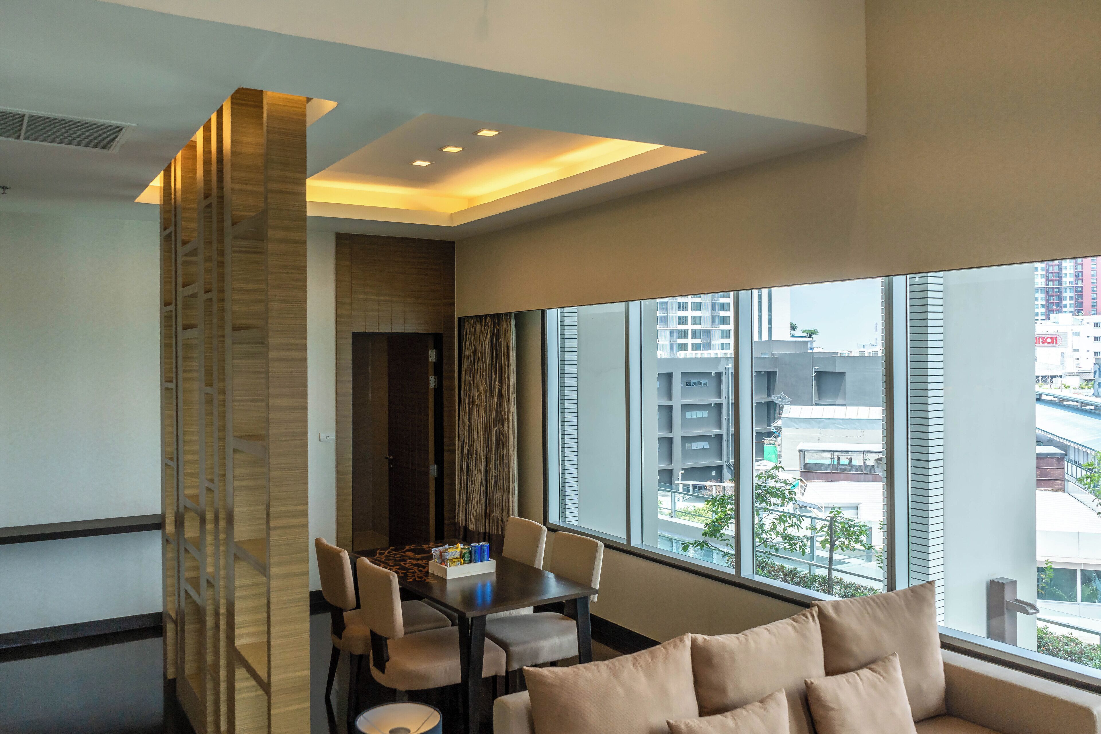 A modern hotel room with a dining area, large windows with a city view, and a cozy seating area.