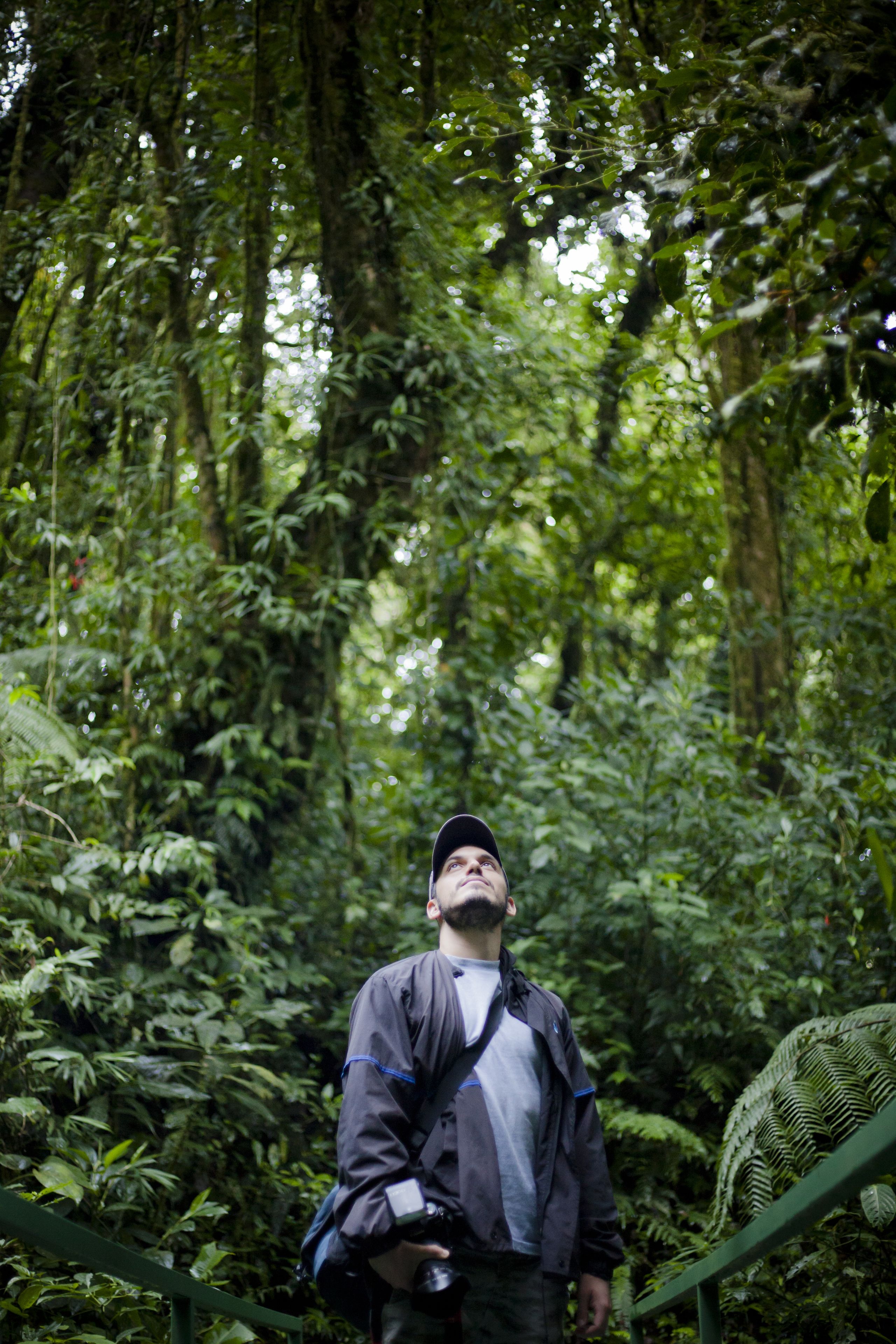 A person standing in a lush, green forested area with dense foliage and a visible metal railing.