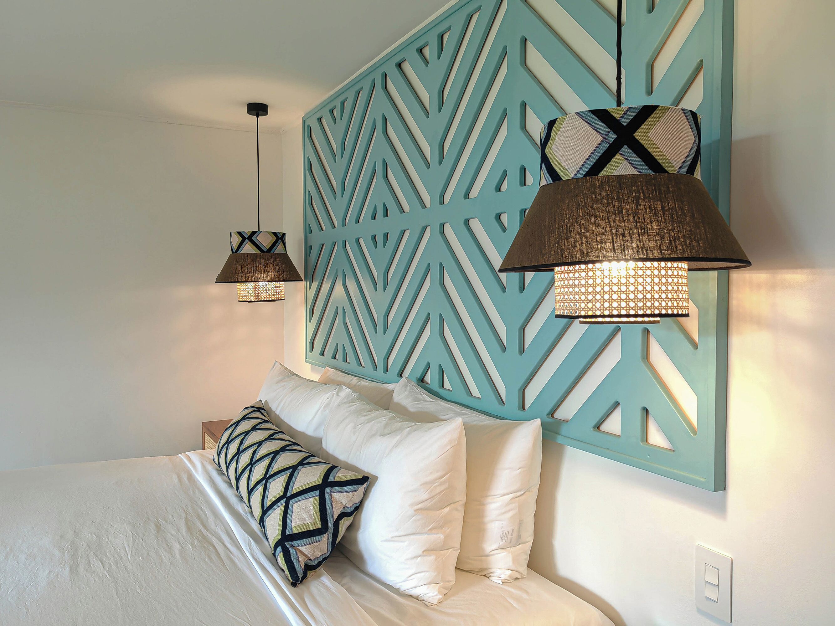 A bedroom with a bed, two hanging lamps, and a decorative wall panel.