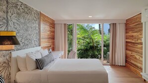 Une chambre moderne avec un grand lit, un bureau et une vue sur une végétation luxuriante, visible à travers une porte-fenêtre coulissante.