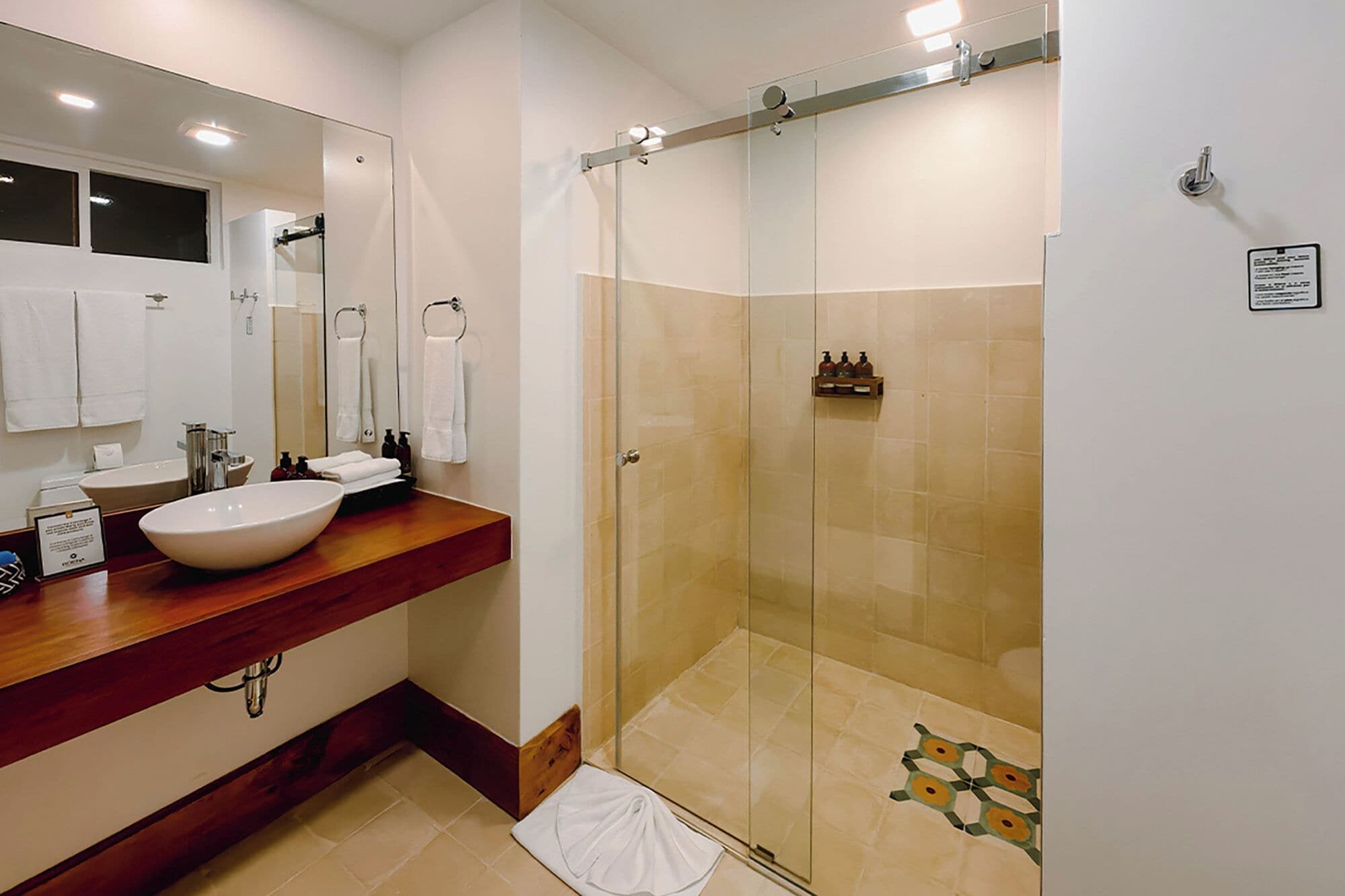 A modern bathroom with a large mirror, two sinks, a shower enclosure, and a wooden vanity.