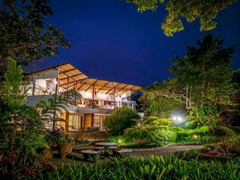 Una casa moderna con un porche cubierto, rodeada de abundante vegetación y un jardín cuidado.
