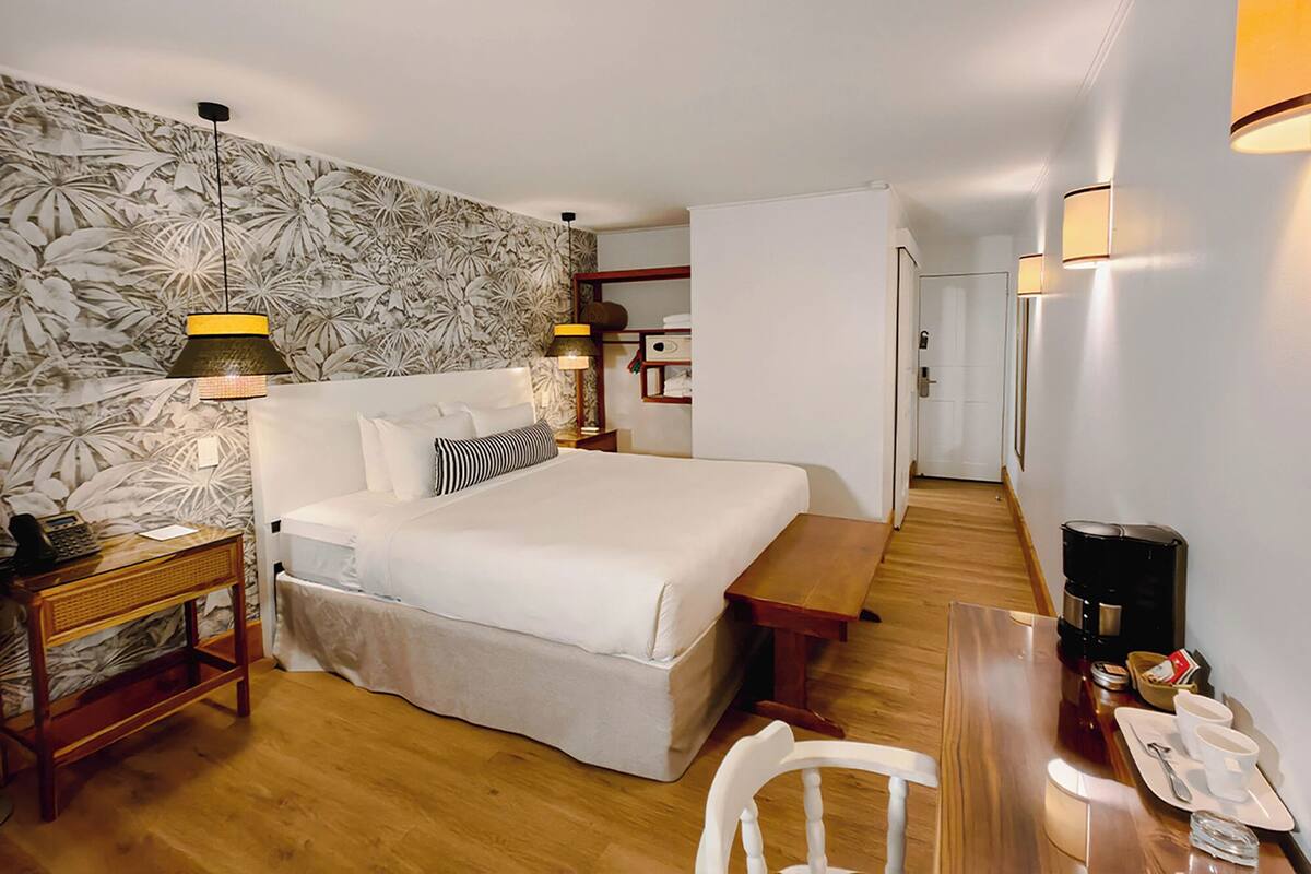 Ein Hotelzimmer mit Bett, Nachttischen, Schreibtisch mit Stuhl, Lampe und Wand mit Blumenmuster.
