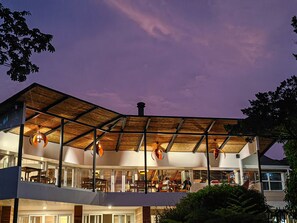 A modern building with a flat roof, large windows, and a covered outdoor seating area. - Monteverde Lodge by Böëna (Monteverde)