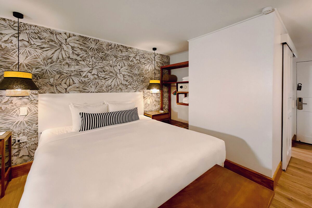 A hotel room with a large bed, two bedside lamps, a wooden nightstand, a wardrobe, and a floral wallpaper.