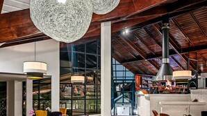 Un hall d’entrée spacieux, doté de meubles modernes, de grandes fenêtres et d’un plafond haut avec des poutres apparentes.