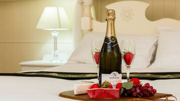 A bottle of Nepenthe champagne, two glasses with strawberries, a slice of red fruit cake, and grapes on a wooden board on a bed.