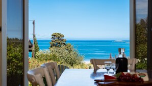 A dining area with a table set for two, overlooking a coastal view with a clear sky and a distant island.