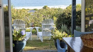 A patio with white chairs, a table, and a view of the ocean.