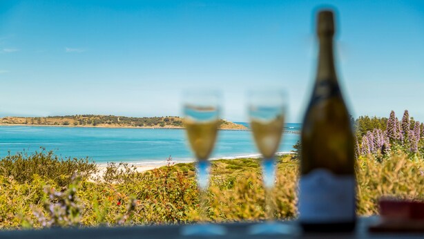 A scenic view of a coastal landscape with a bottle and two glasses of wine on a table.