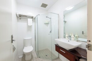 A modern bathroom with a glass-enclosed shower, a white toilet, and a vanity with a mirror and toiletries. - Adabco Boutique Hotel Adelaide (Adelaide)