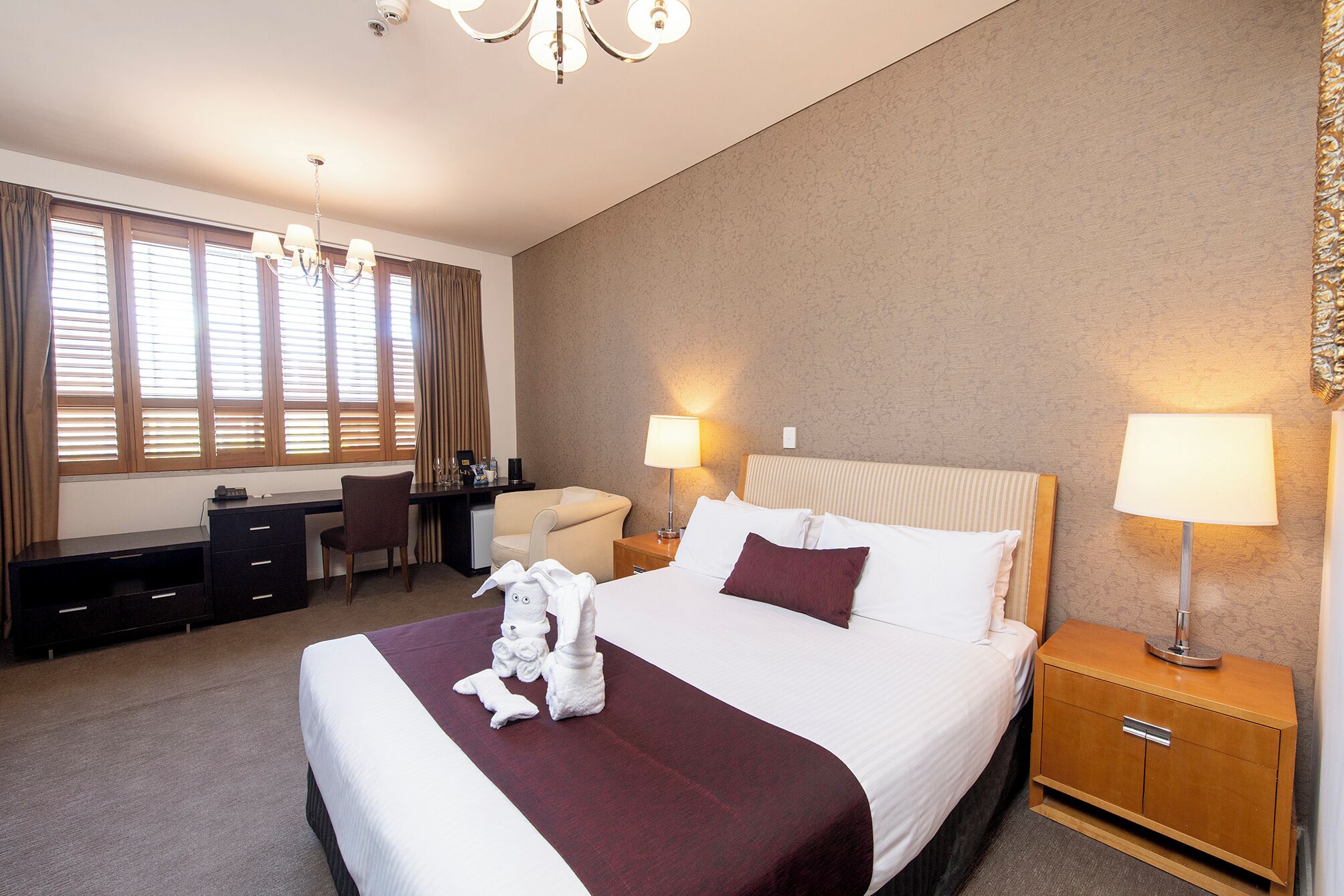 A hotel room with a large bed, two bedside lamps, a desk with a chair, and a small table.