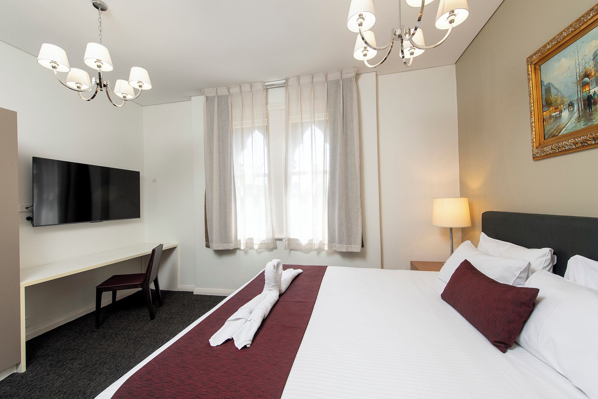 Een hotelkamer met een bed, bureau, televisie en een schilderij aan de muur.