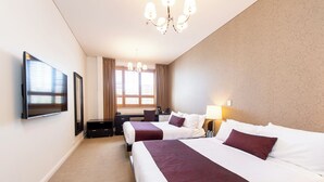 Een hotelkamer met twee bedden, een bureau, een stoel, een televisie en een kroonluchter.