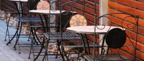 A row of outdoor tables and chairs against a brick wall with a wooden slatted design.