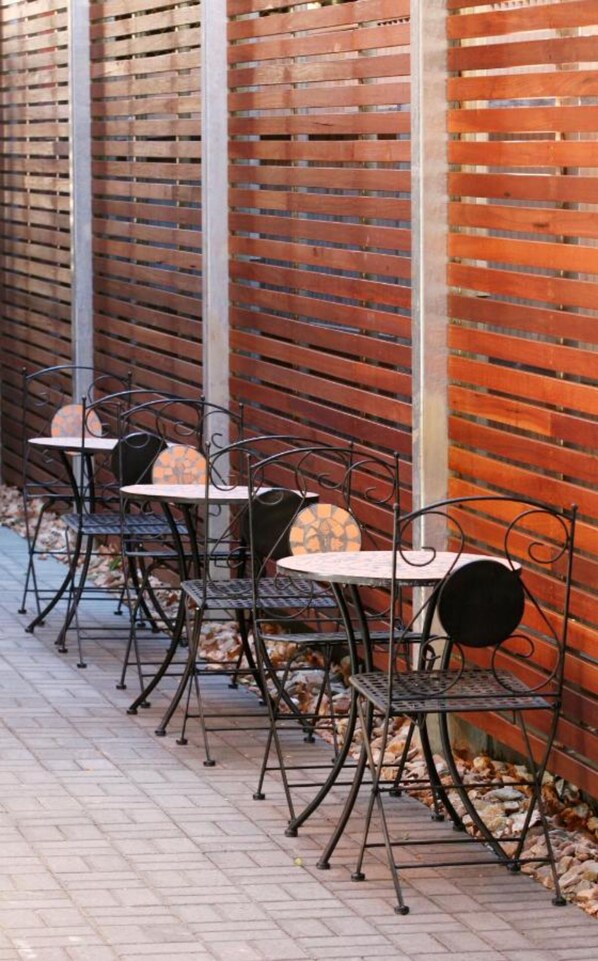 A row of outdoor tables and chairs against a brick wall with a wooden slatted design. - Adabco Boutique Hotel Adelaide (Adelaide)