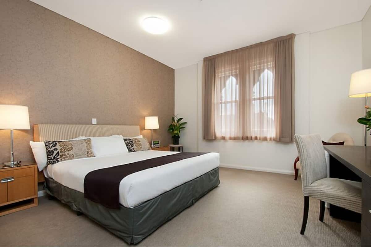 A hotel room with a large bed, bedside lamps, a desk, and a chair.