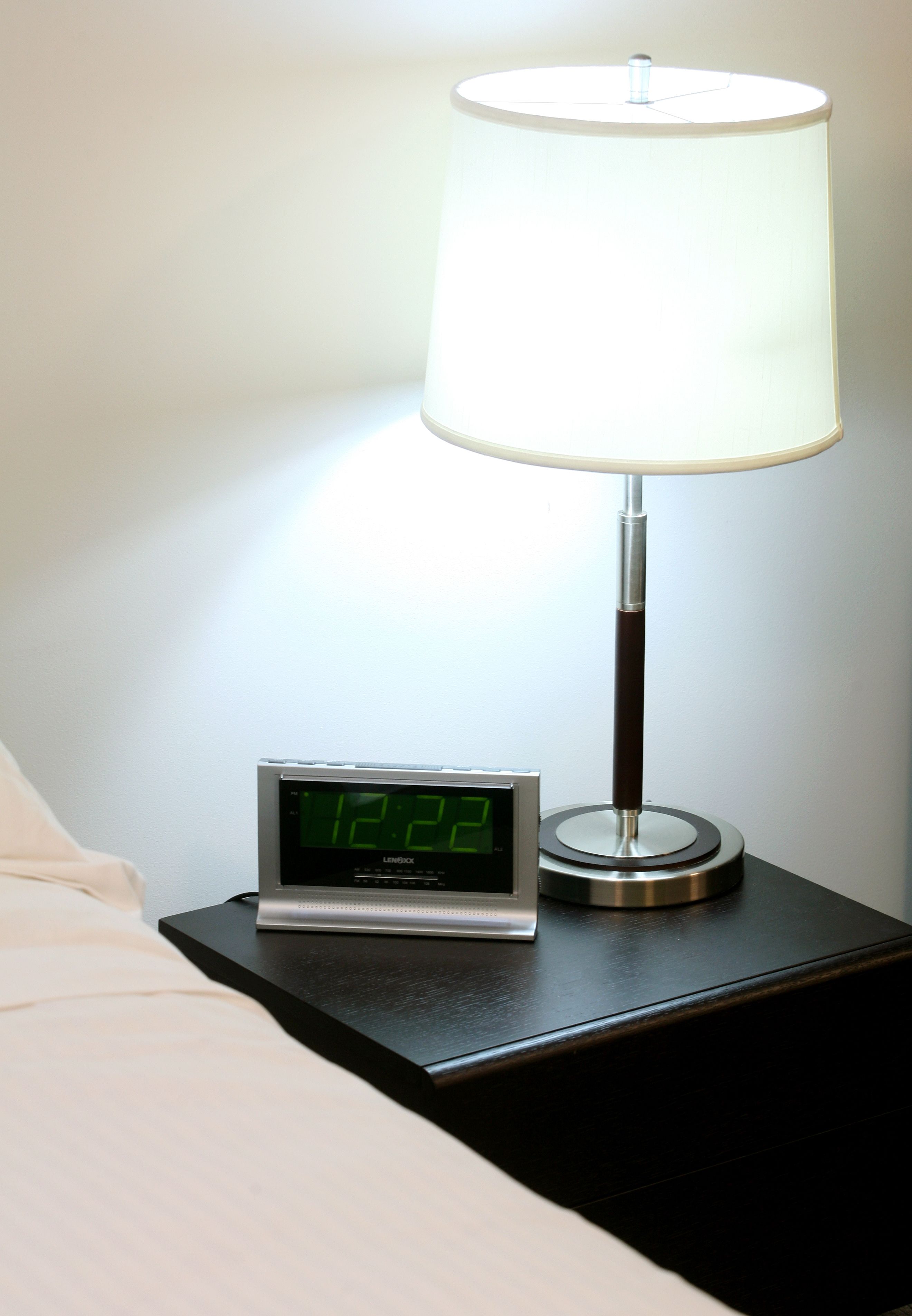 A bedside table with a digital clock and a lamp.
