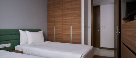 Un dormitorio con dos camas, un cabecero verde, un armario de madera y una puerta que da a otra habitación.