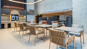 Un restaurante moderno con sillas y mesas de madera, una zona de cocina y una lámpara colgante grande.
