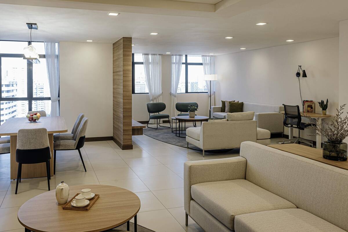 A modern living room with a dining area, a sofa, a coffee table, and a large window with curtains.